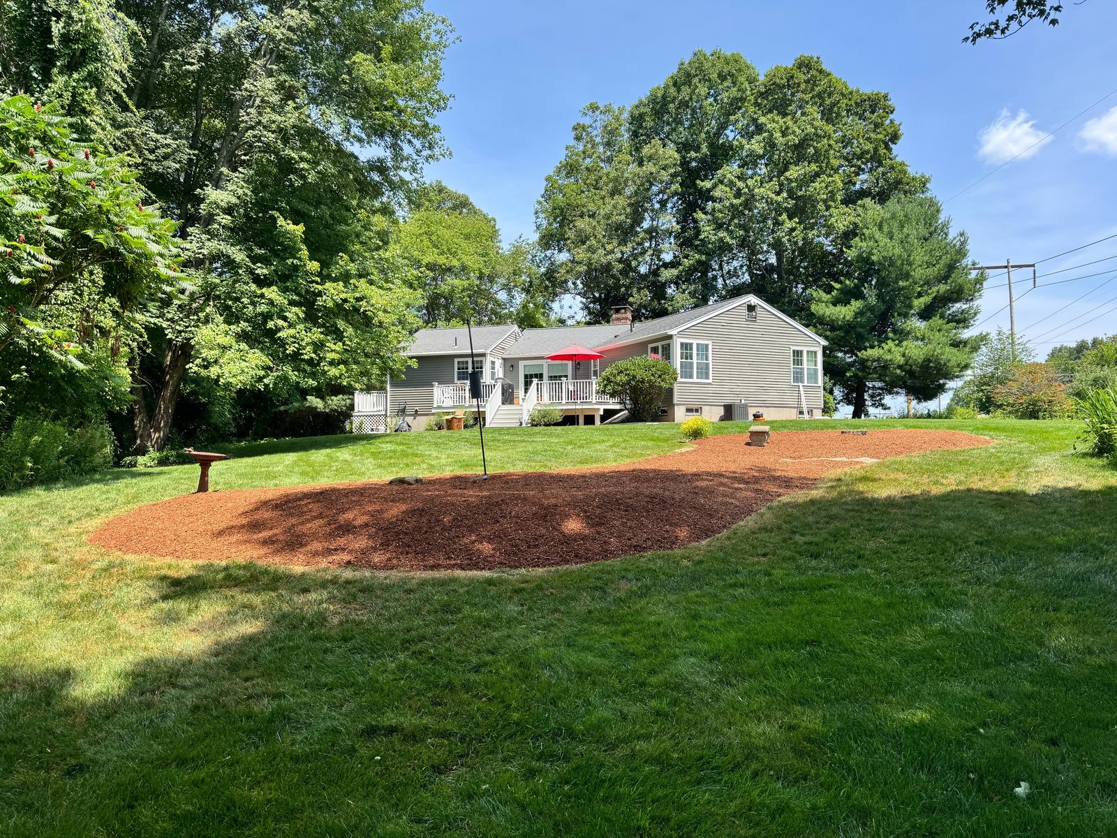 Red mulch bed in a wide lawn with a ranch house in the background